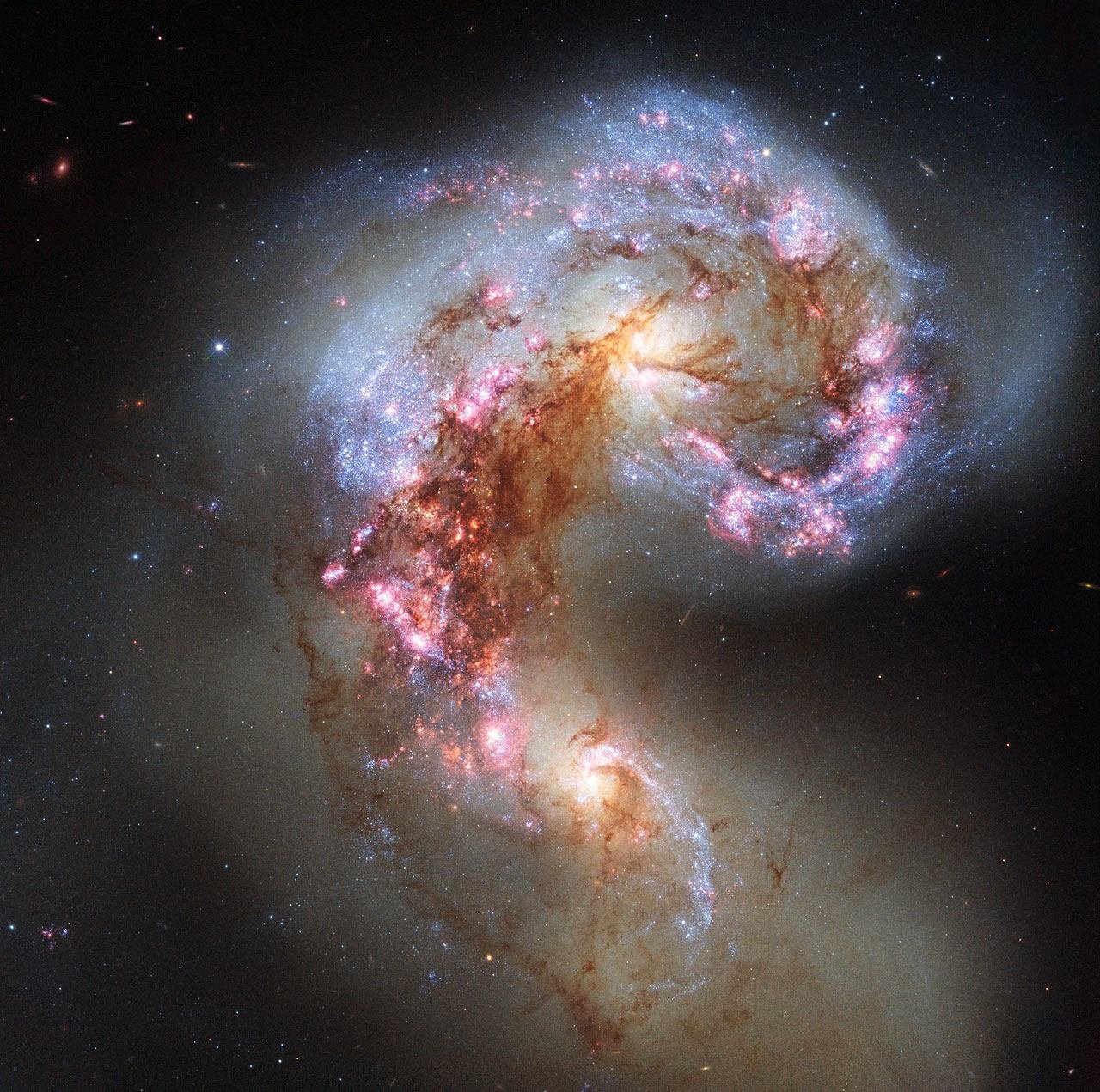 The Antennae Galaxies, two spiral galaxies colliding in a swirl of stars and glowing pink star-forming regions